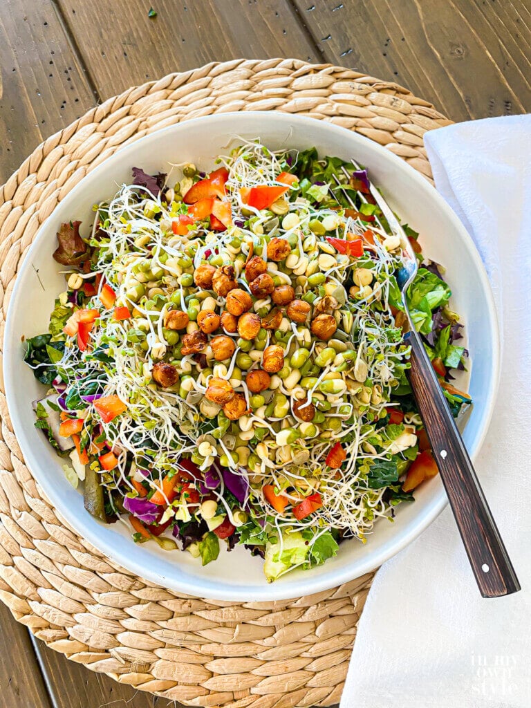 Dinner table set up with a plate of chopped salad with roasted chickpeas, sprouted mung beans, lentils and broccoli sprouts on top.