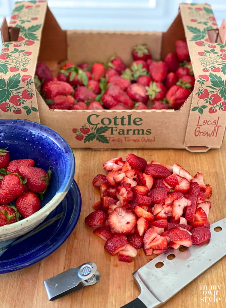Box of fresh picked strawberries on cutting board with knife.