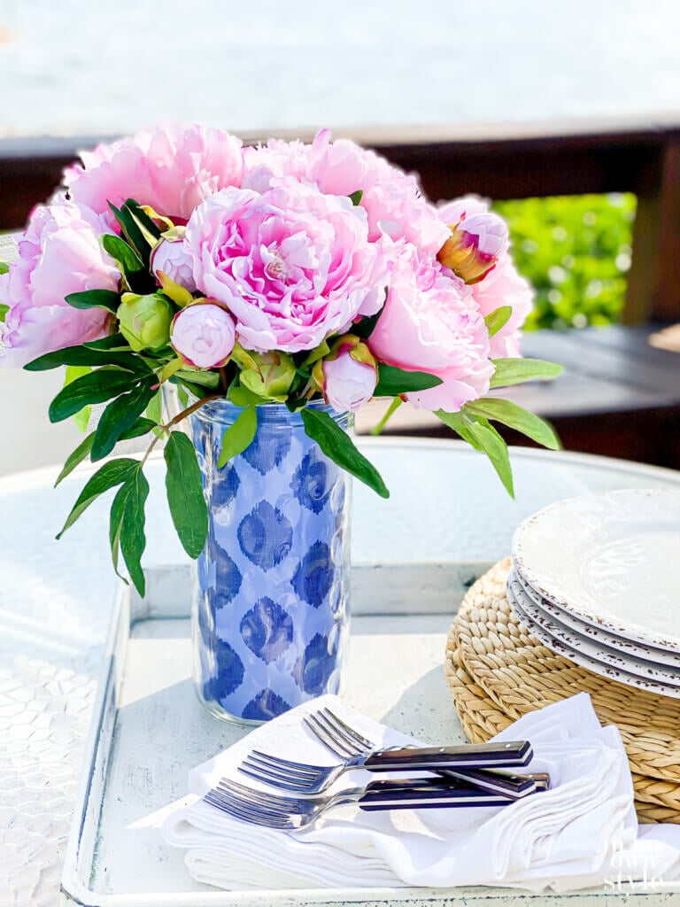 Pink peonies in a tall glass vase with two-tone blue pattern gift wrap wrapped around it.