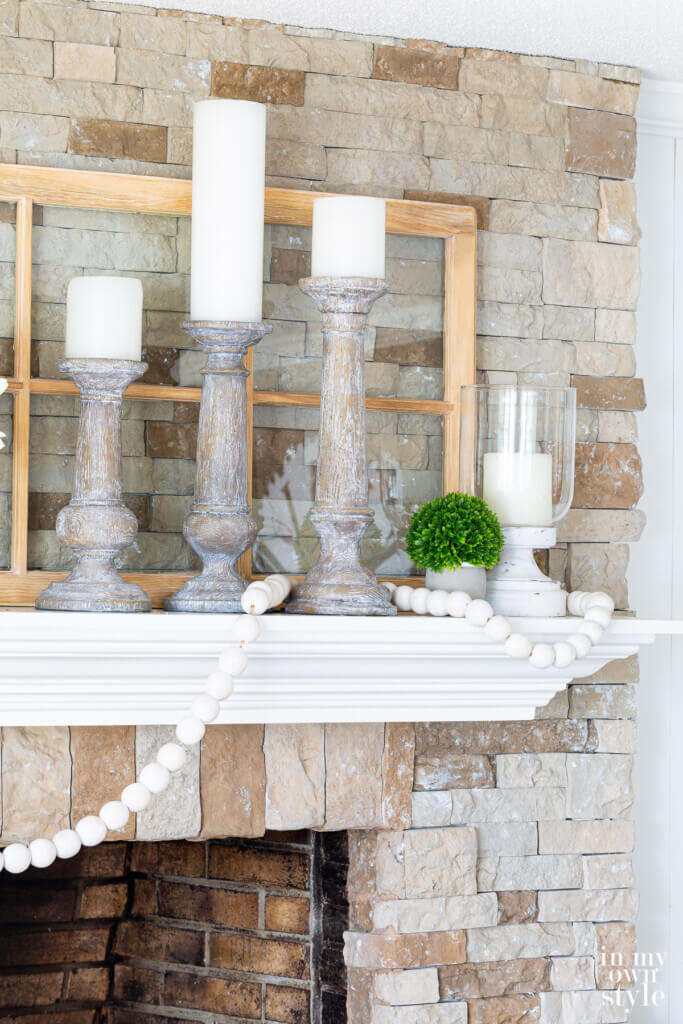 3 large white-washed wood candle holders with white pillar candles decorating a fireplace mantel.