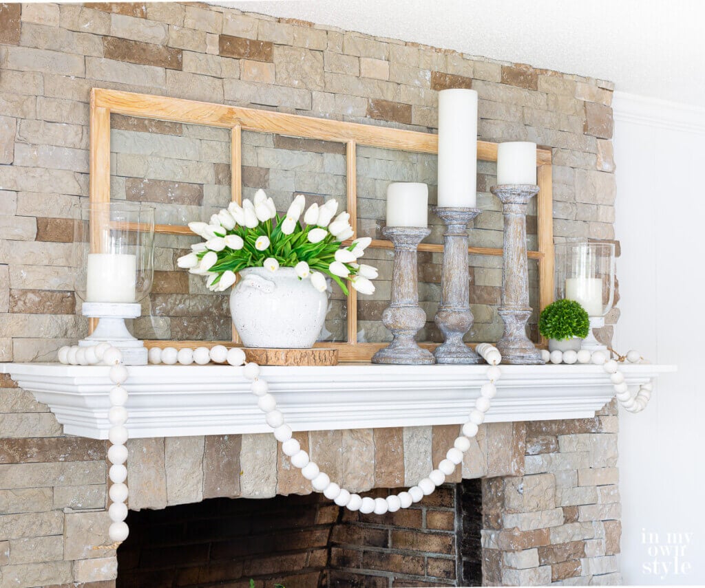 White and green summer themed mantel decor on a stone fireplace.