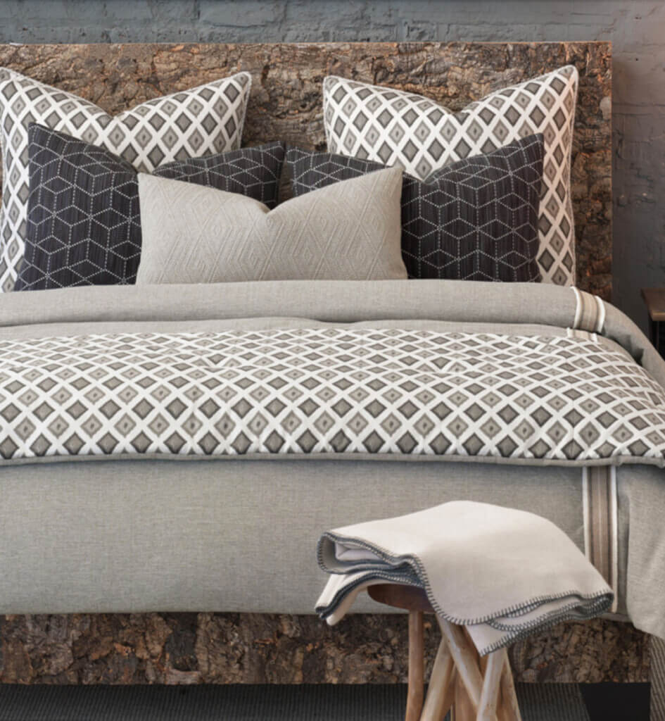 Brown and white bedding on bed with decorative pillows and shams that have a karate chop dent on the top.