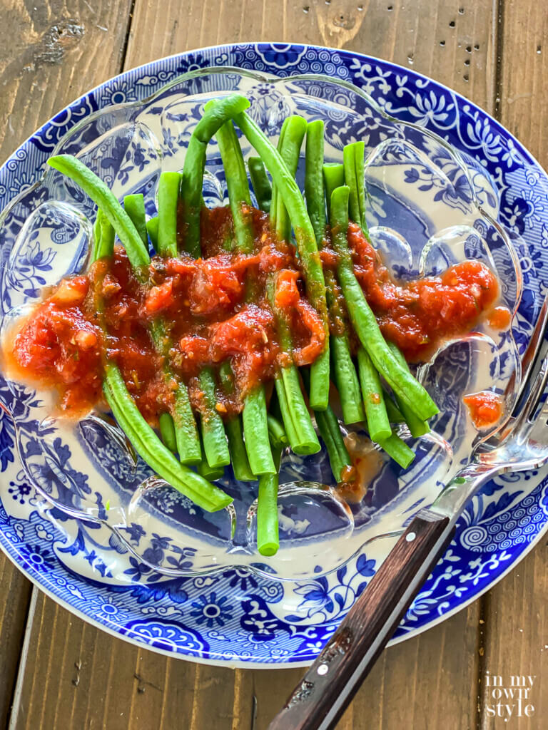 Plate of green string beans with plant based on oil tomato dressing drizzles over them.