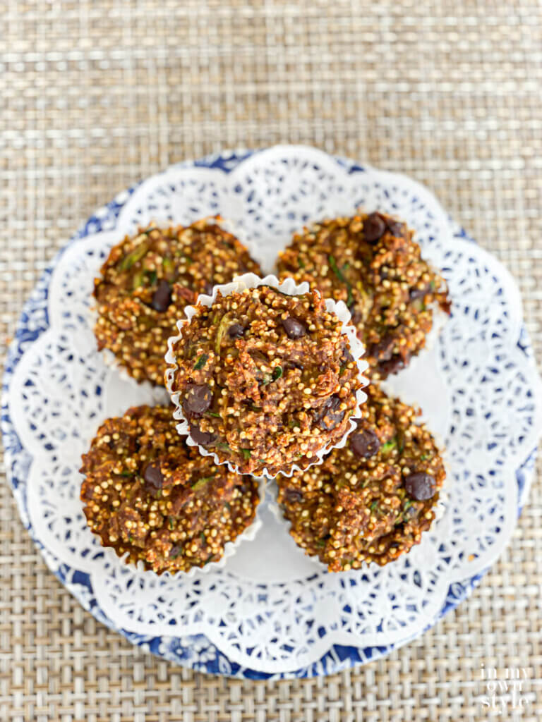 Vegan no-oil zucchini muffins stacked on a doily covered blue and white plate.