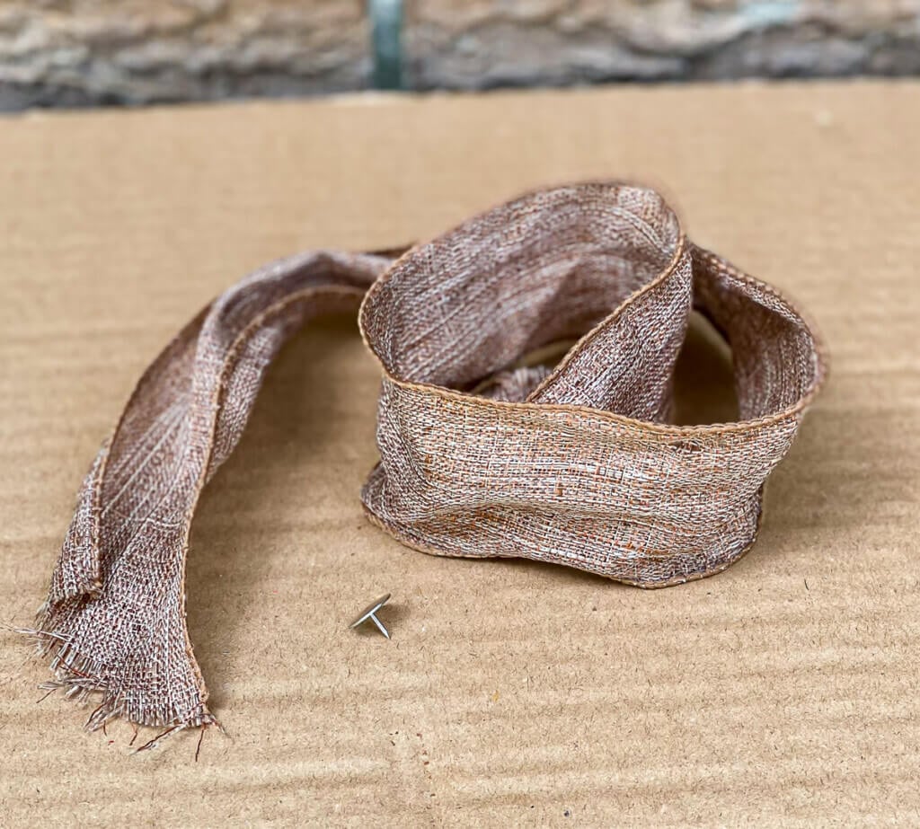 ribbon and a thumb tack used to hang a flat basket on a door.