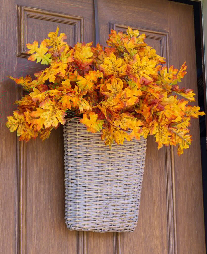 flat sided hanging basket on door filled with leaves for fall decoration.