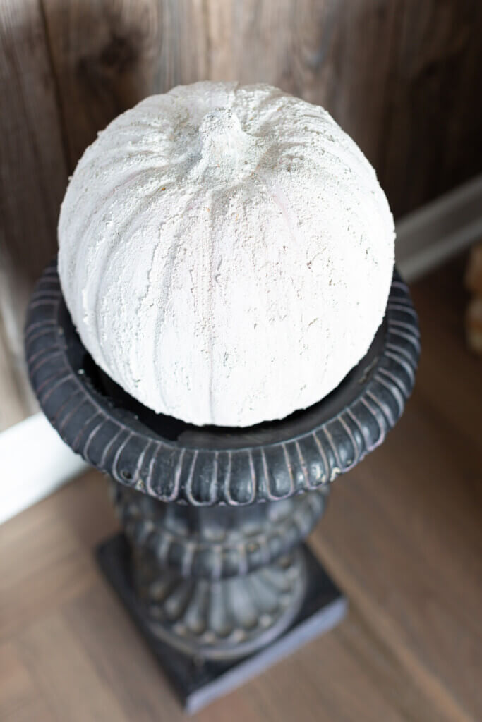 Neutral fall decorating colors for fall. Cement covered plastic pumpkin on black pedestal urn.