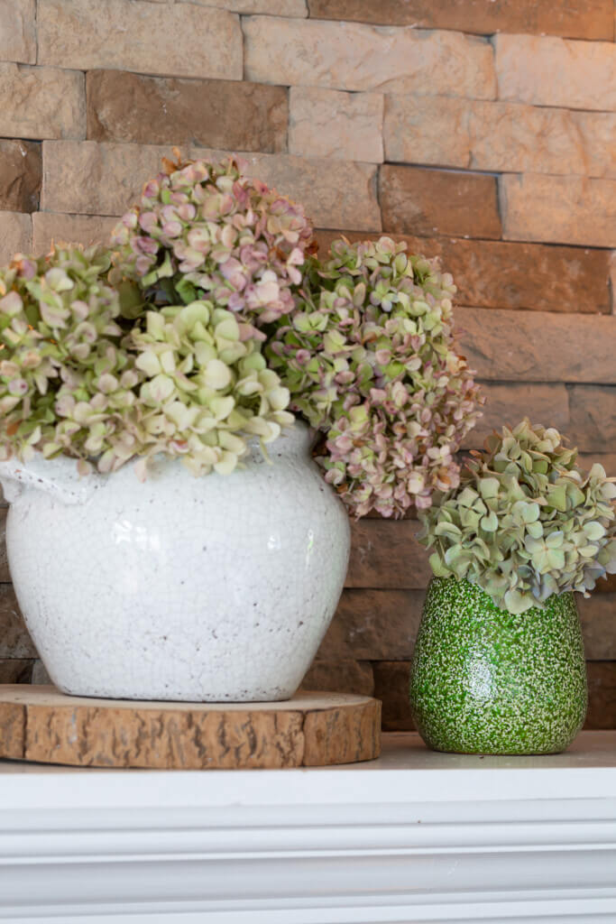 Dried hydrangeas in planters on a fireplace mantel.