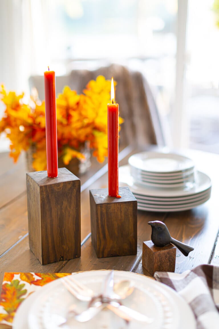 Completed DIY Wooden Candle Holders on a dining table with dark orange taper candles.