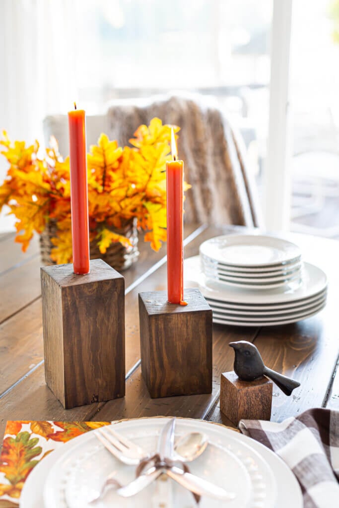 Completed DIY Wooden Candle Holders on a dining table with dark orange taper candles.