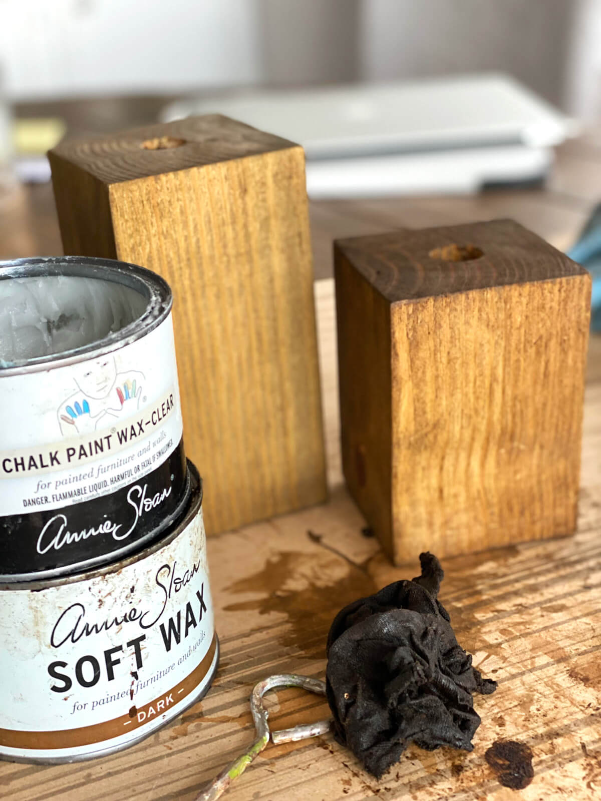 Clear and dark wax cans shown in front of stained wood blocks made into DIY wooden candle holders.