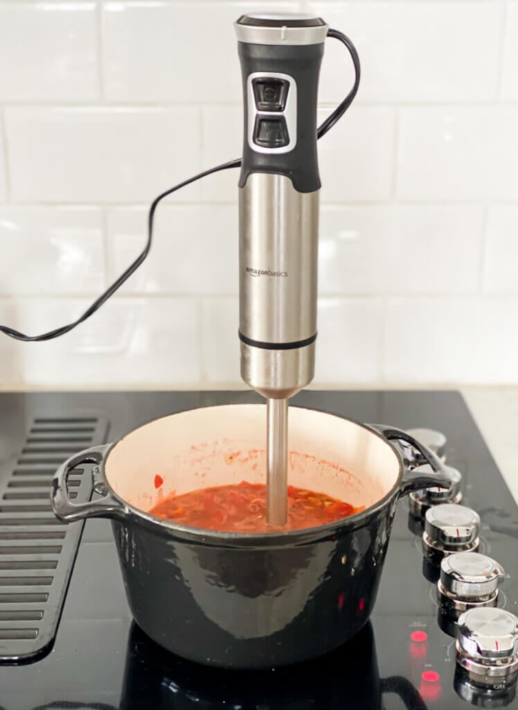an immersion blender in a soup pot that is cooking on a stove