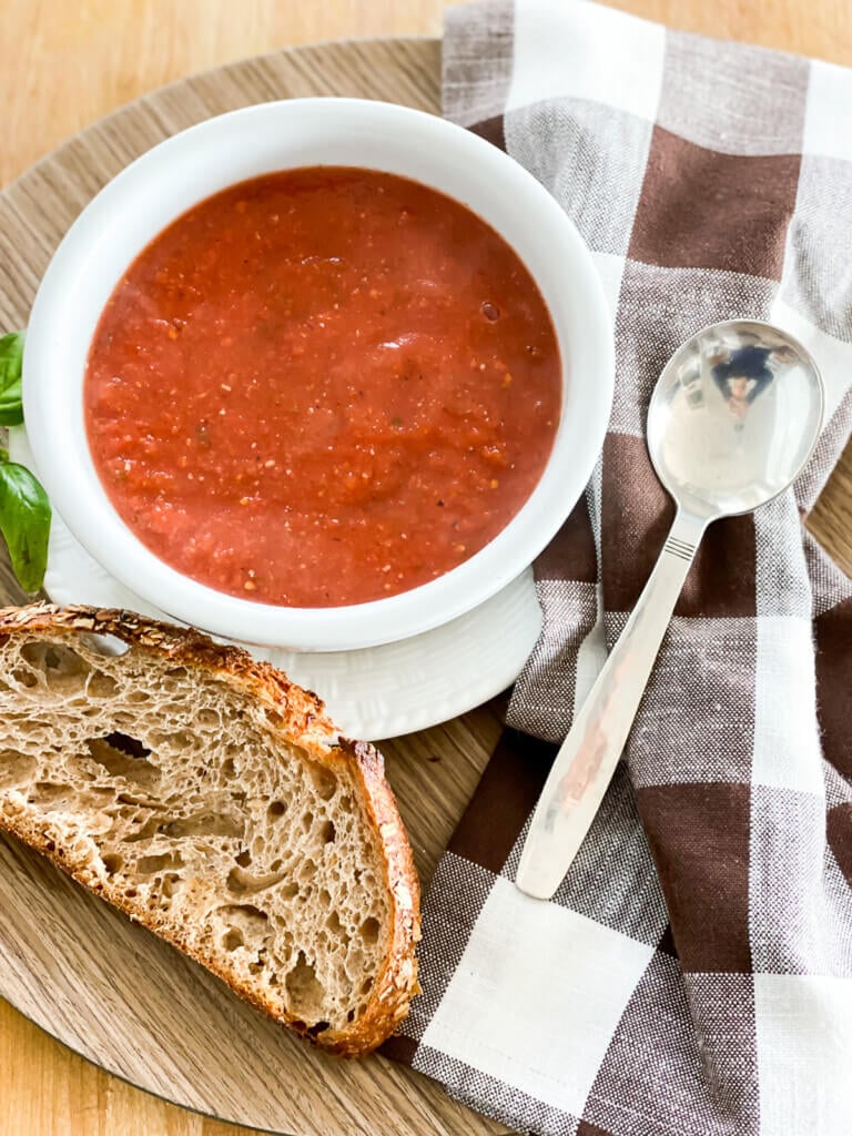 A tray with a lunch of vegan tomato soup, crusty bread a napkin and spoon.