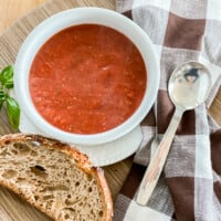 A tray with a lunch of vegan tomato soup, crusty bread a napkin and spoon.