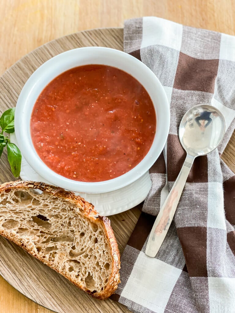 A tray with a lunch of vegan tomato soup, crusty bread a napkin and spoon.