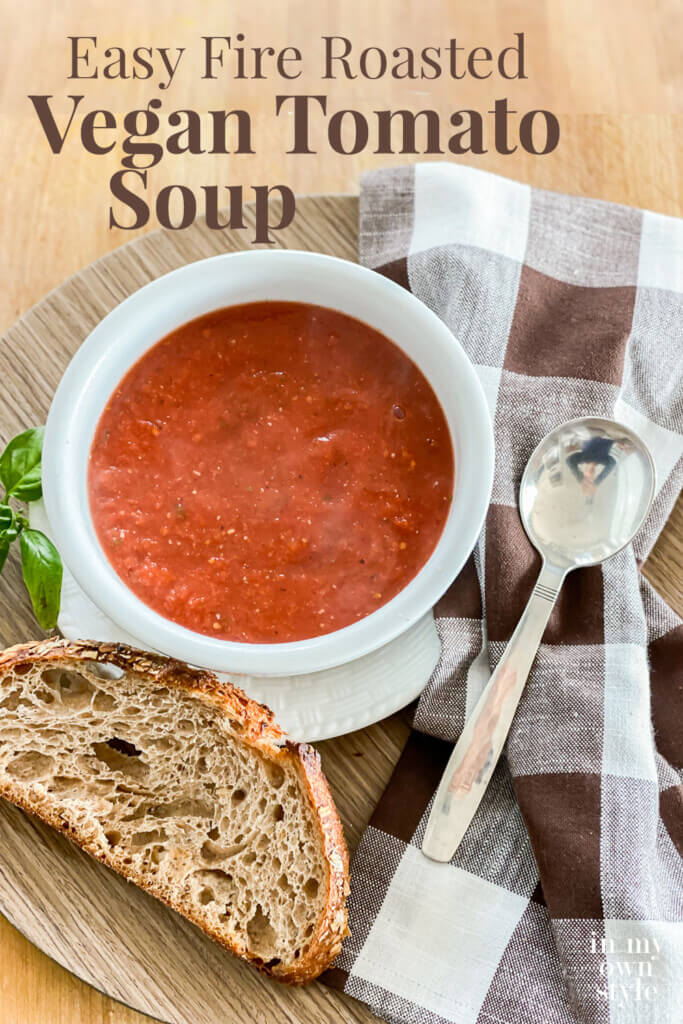 Bowl of soup and slice of crusty bread on a tray. Text overlay says Easy fire roasted vegan tomato soup.