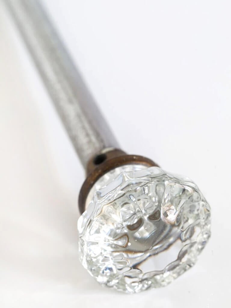 Glass doorknob attached to metal pipe to create DIY curtain rods.