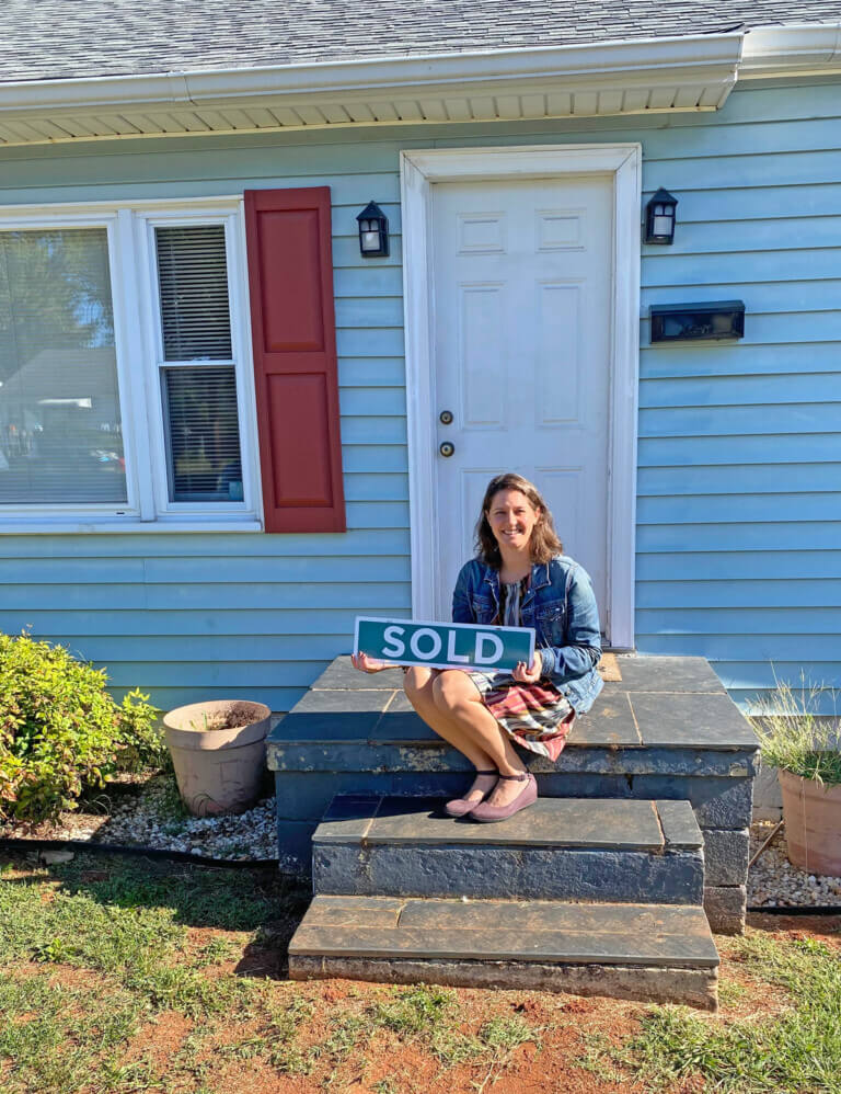 girl sitting on house steps with Sold sign in her hand.
