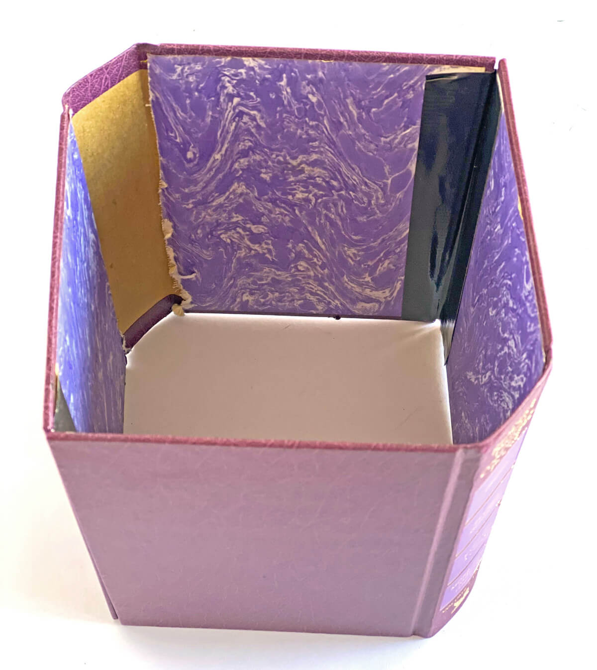 Two books taped together to make a decorative cover for a plastic planter pot of flowers.
