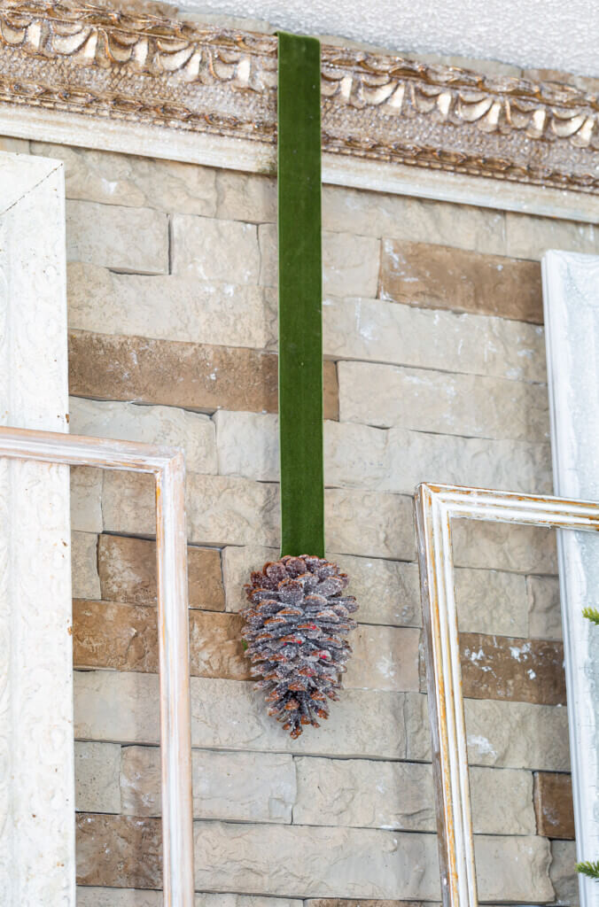 Green velvet ribbon with glittered pinecone attached hanging from ornate gold frame.