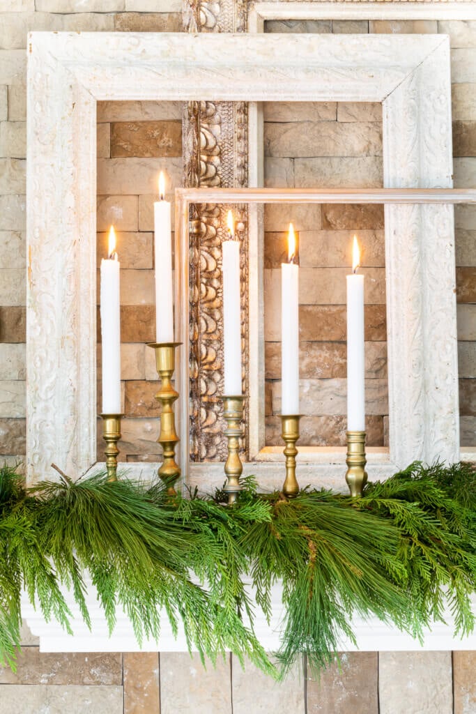 A group of brass candlesticks and white candles on mantel decorated for Christmas