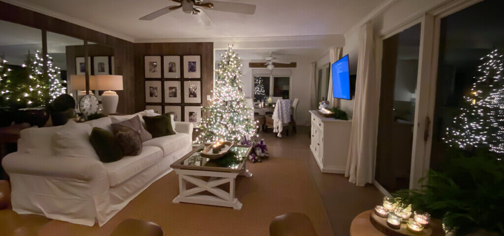 Wide angle shot at night of living room that looks like there are 4 Christmas trees in reflections.