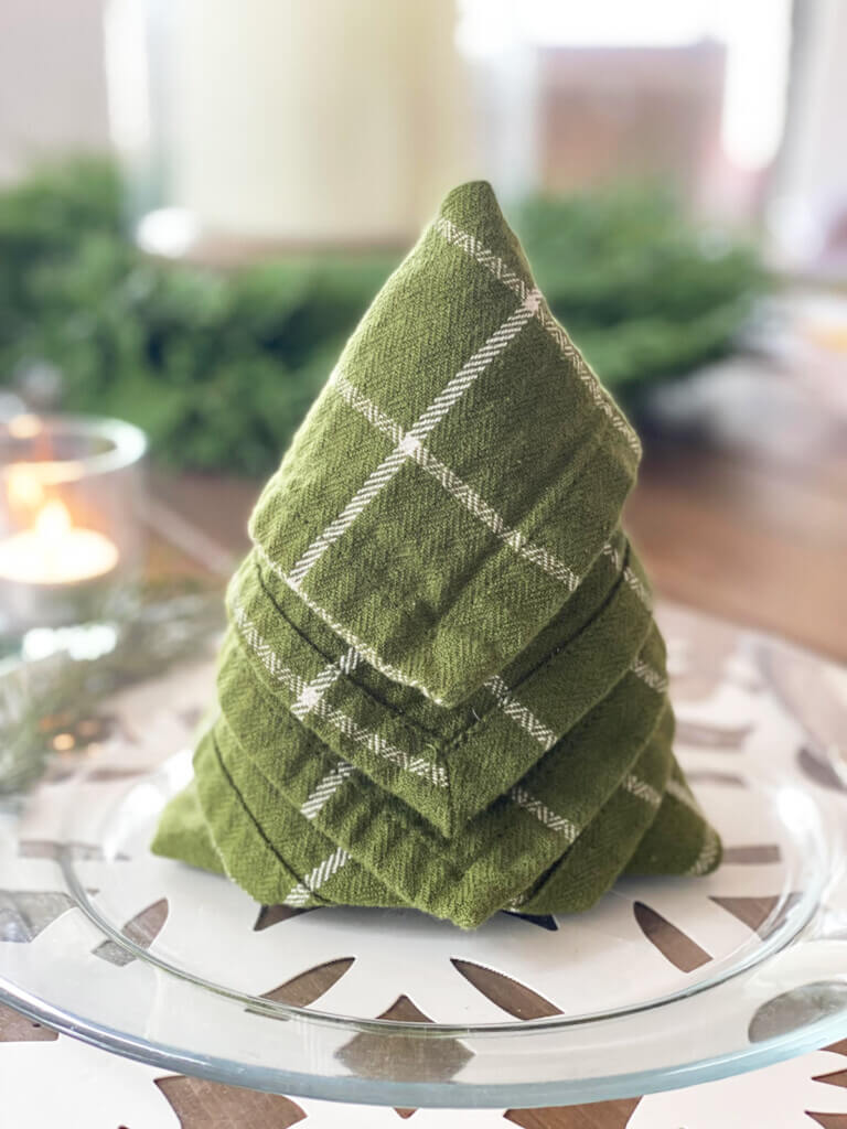 Green and white napkin on a dinner plate that is folded to look like a Christmas tree. 