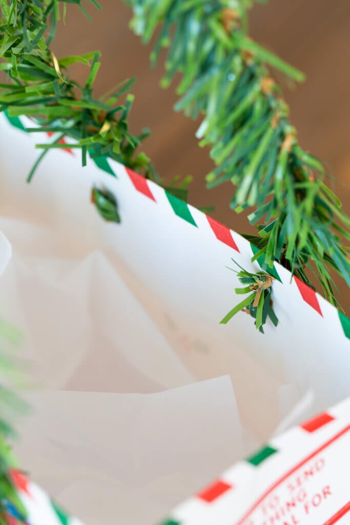 how to attach a pine garland tie to a gift bag to make a handle for the bag.