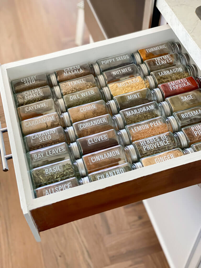 square glass spice jars with labels in a kitchen drawer.