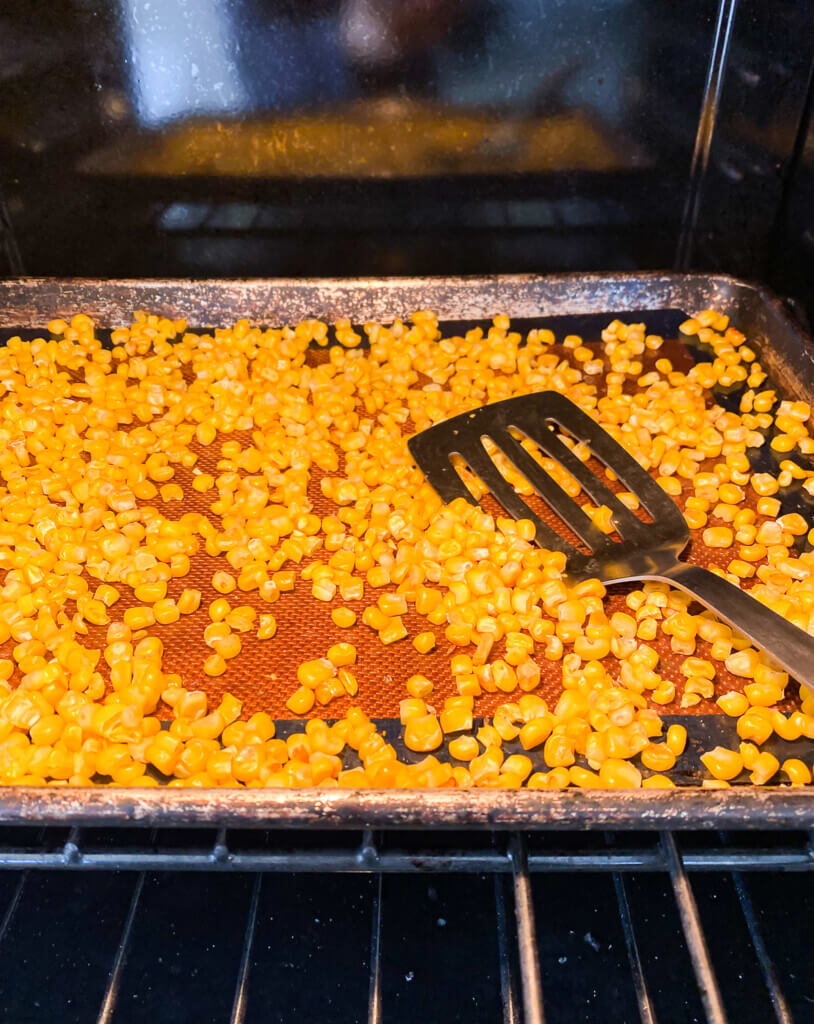 Frozen corn kernels on a baking tray in an over getting roasted.