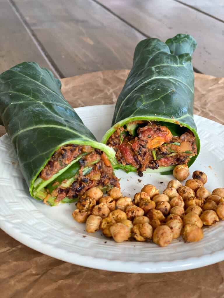 A vegan collard green wrap cut in half on a plate with roasted chickpeas.