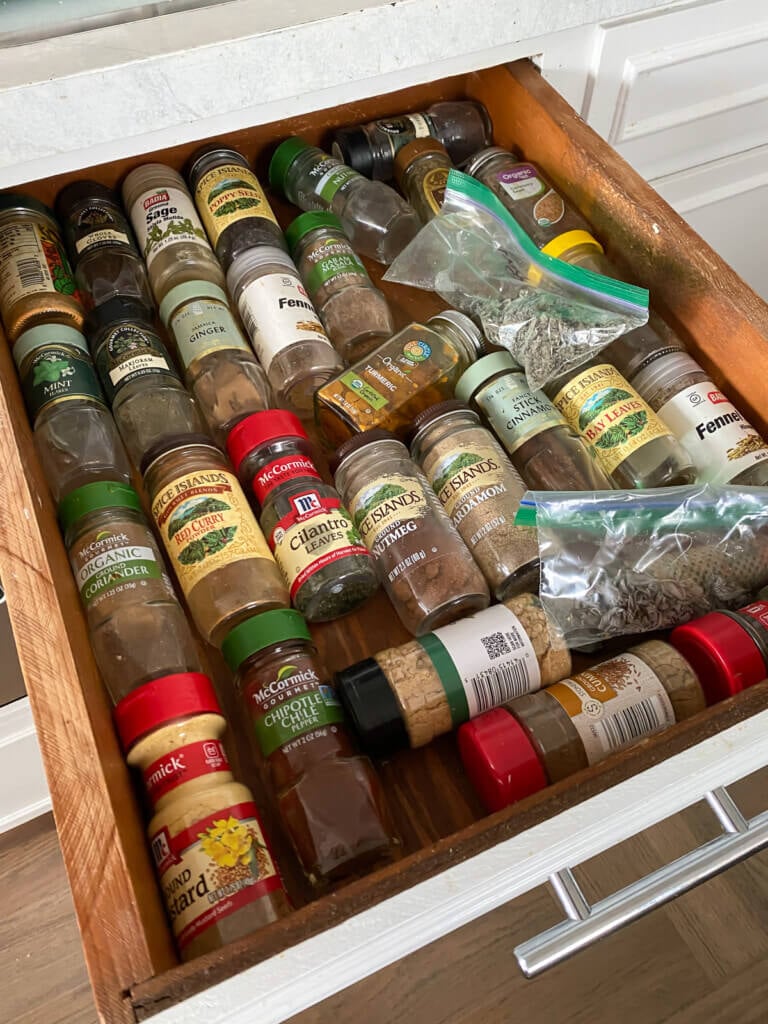 A messy jumble of spice jars in a drawer before it gets an organization makeover.