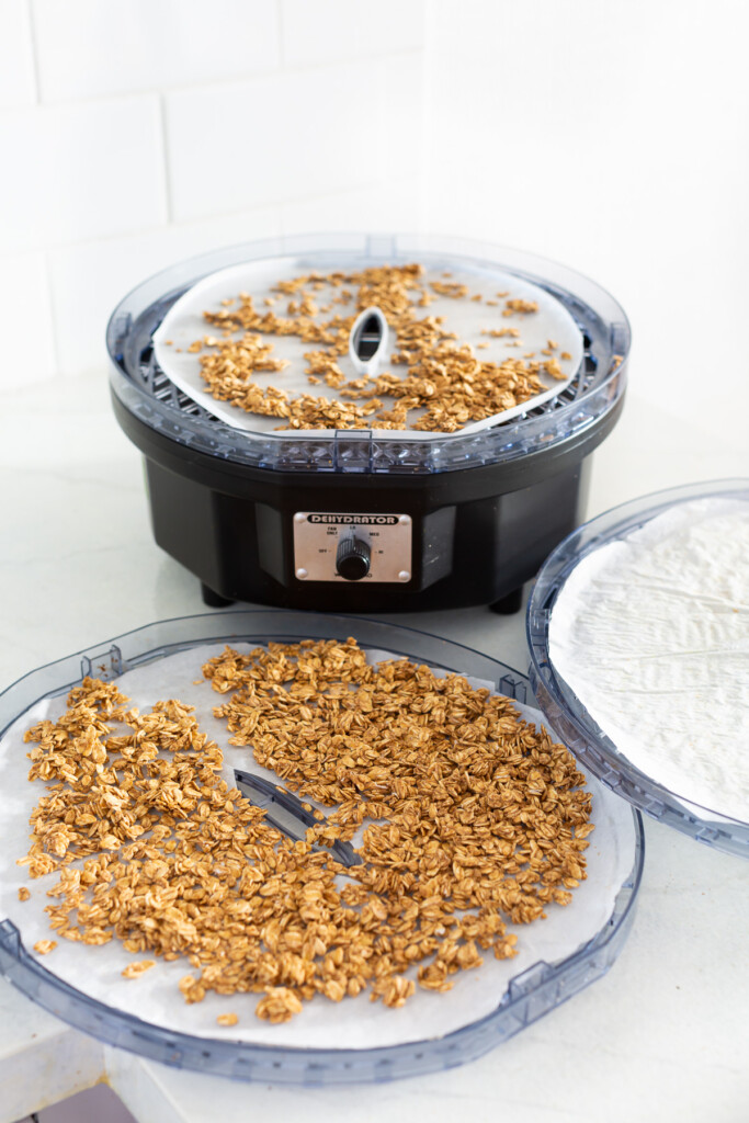 A dehydrator open showing trays with crunchy rawnola being dried.