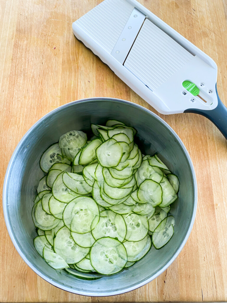 sliced cucumbers in a bowl with a mandoline next to it.