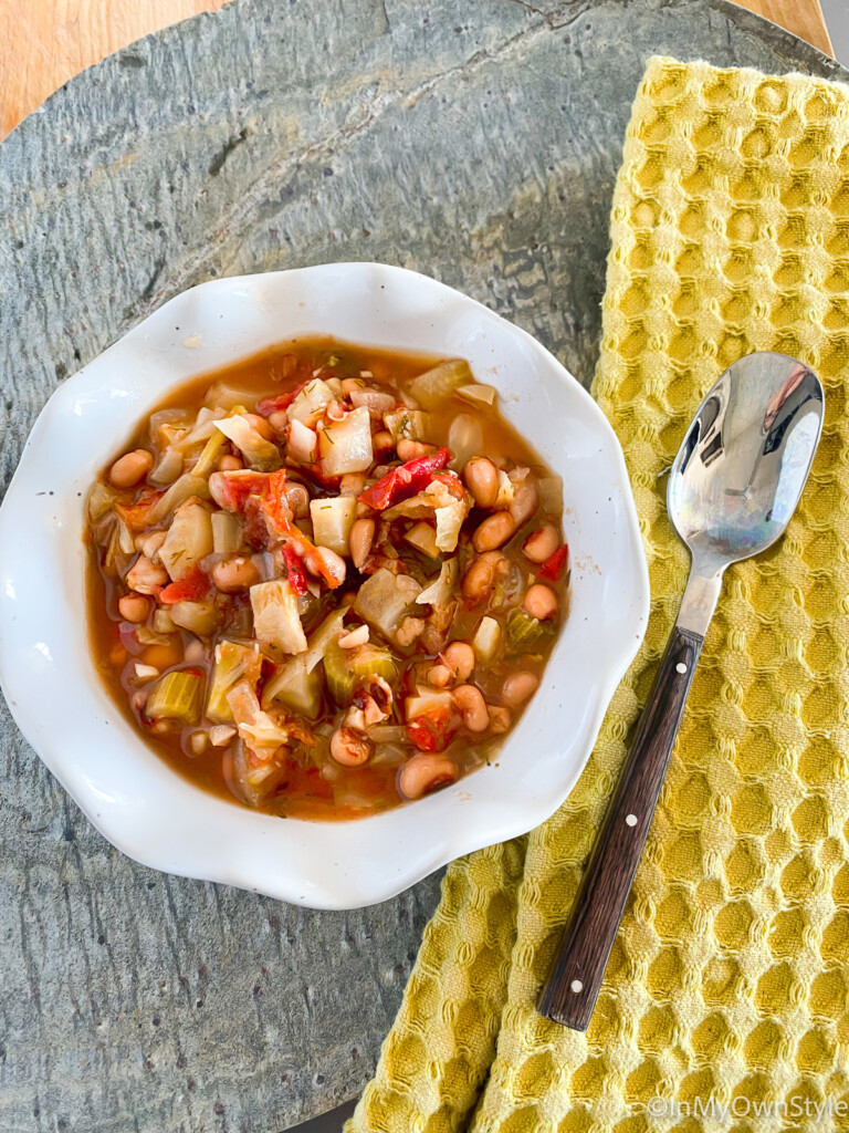 A bowl full of Ikarian stew with a napkin and spoon on the side.