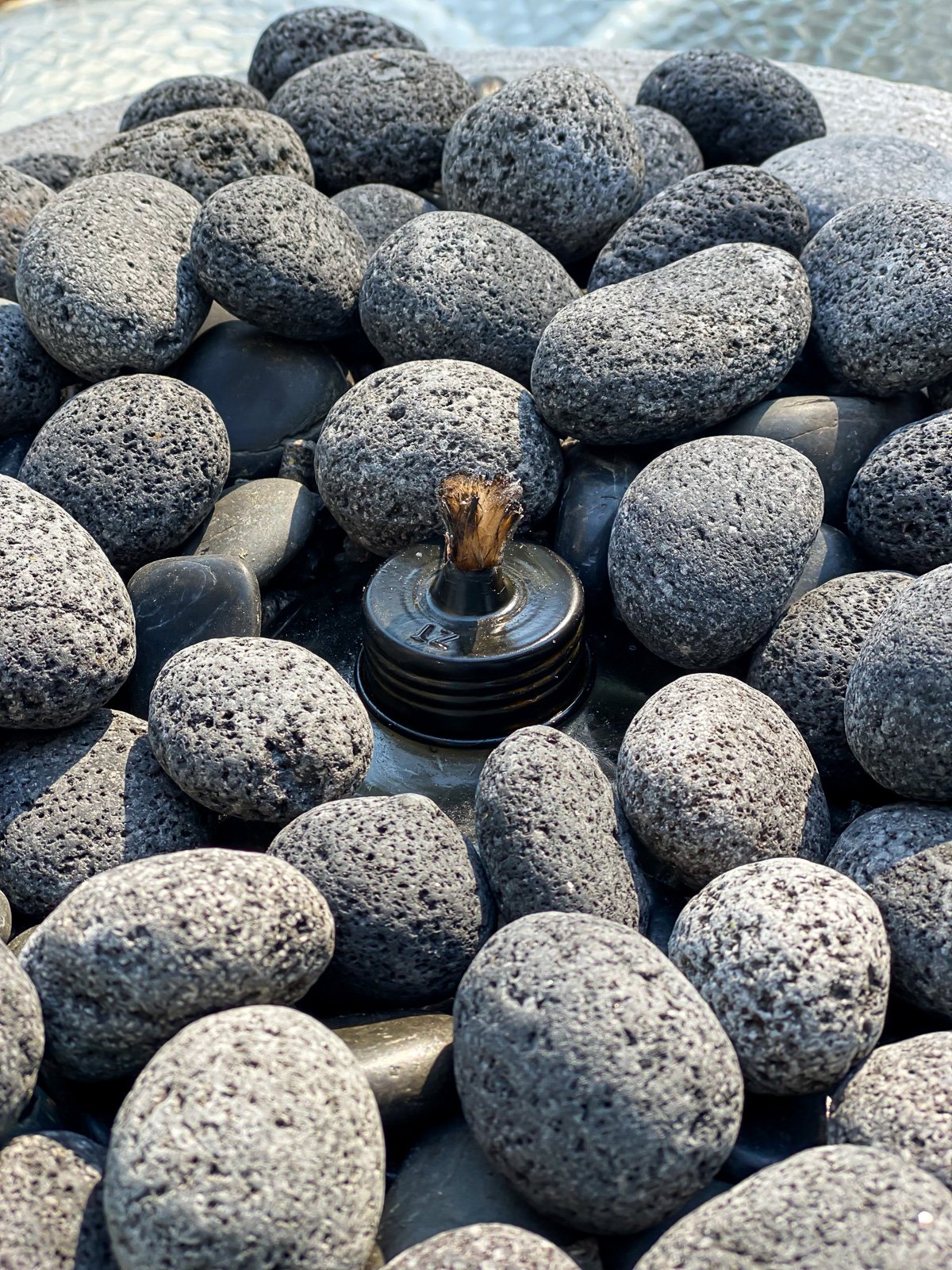Close up of covered tabletop torch in planter filled with stones.