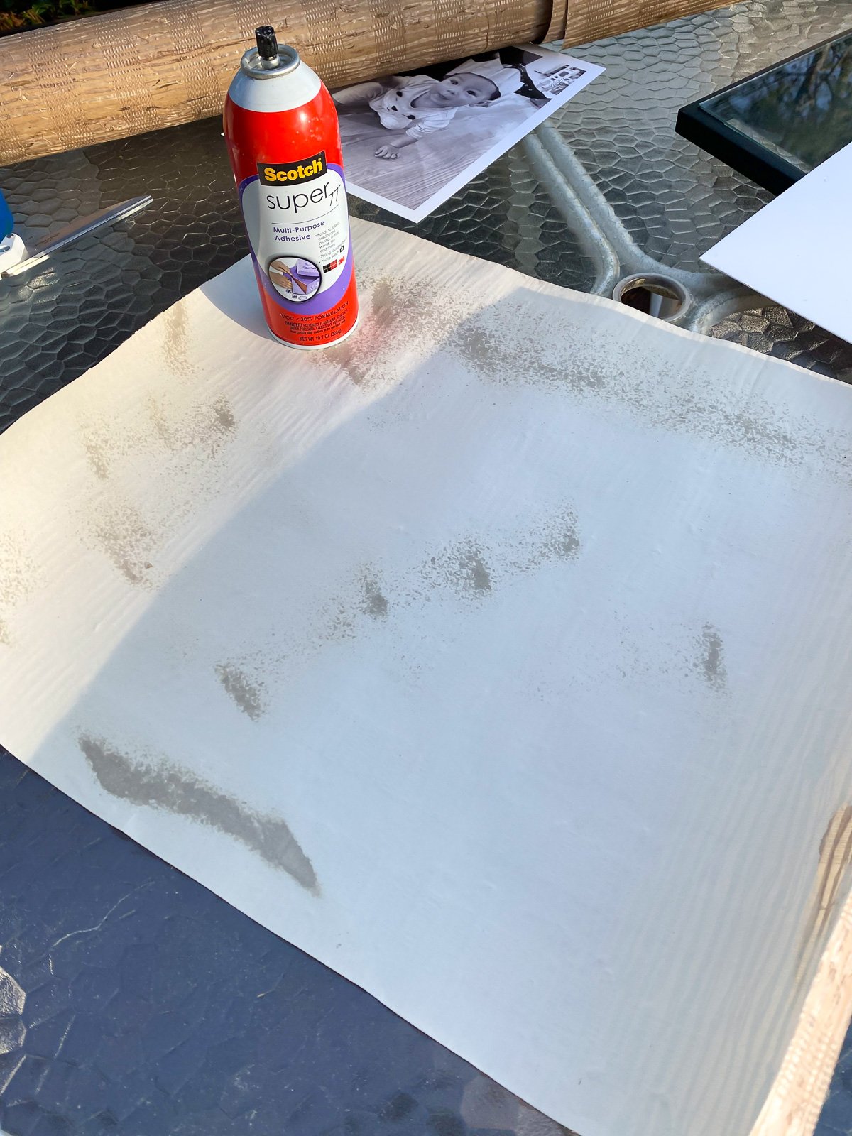 Spraying spray glue on the back of wallpaper to cover a picture frame mat.