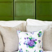 Linen pillow with violets on a sofa with a decorative screen behind it painted green with glaze and dark wax.