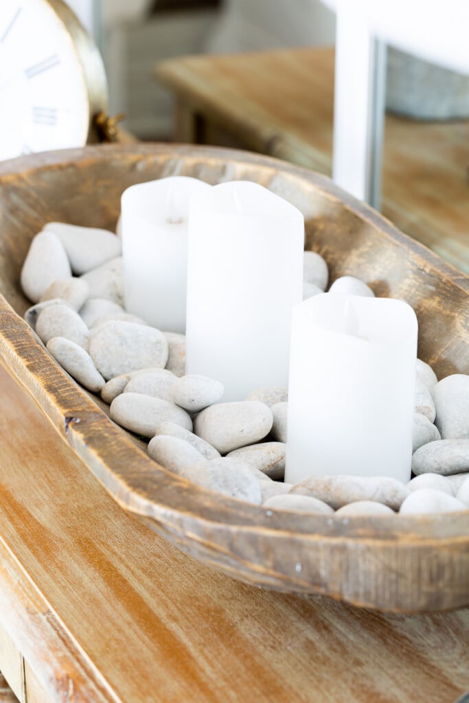 white candles in a dough bowl filled with white rocks on living room table