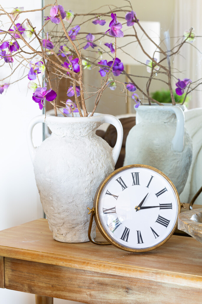 Faux flowers and clock on living room console table.