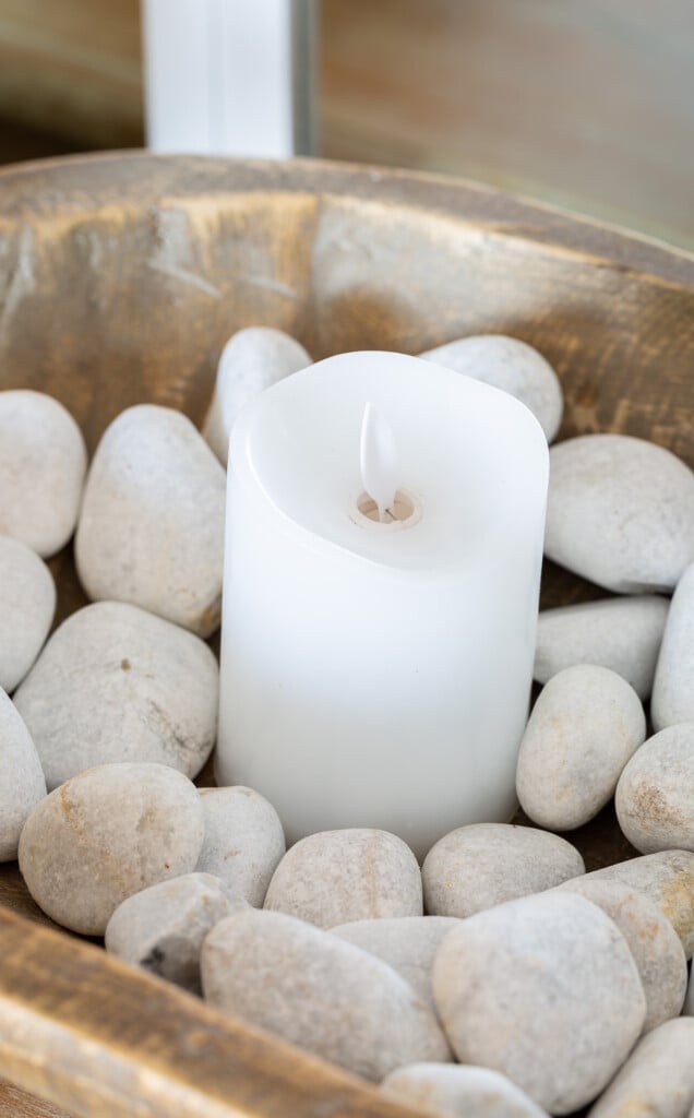 close up of a candle in a dough bowl filled with rocks used to decorate a living room for summer.