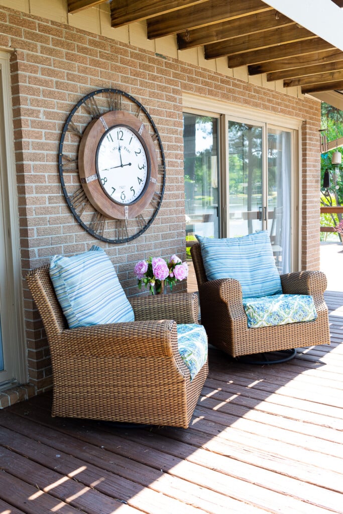 outdoor wall clock hanging on brick wall on a deck.
