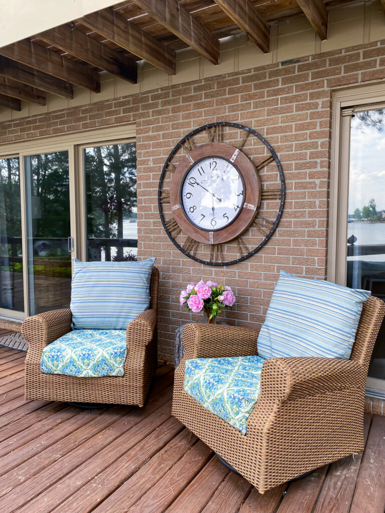 Outdoor deck with rattan furniture and a large wall clock on the wall behind the chairs.