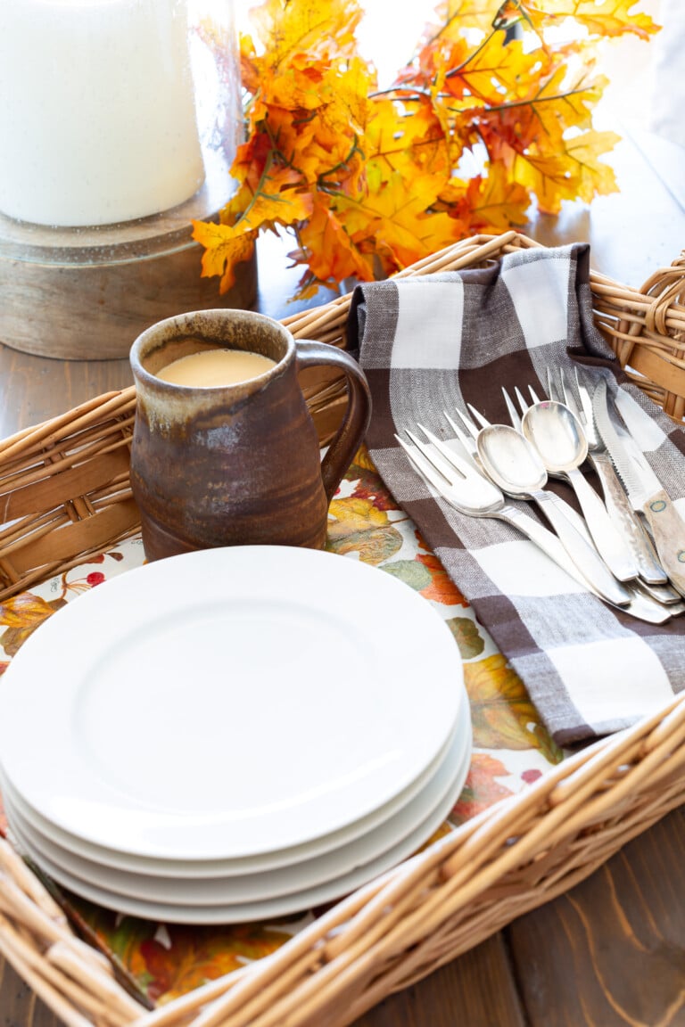 Wicker basket tray completed with autumn leave pattern paper. White plates and brown and white napkin and rustic mug.