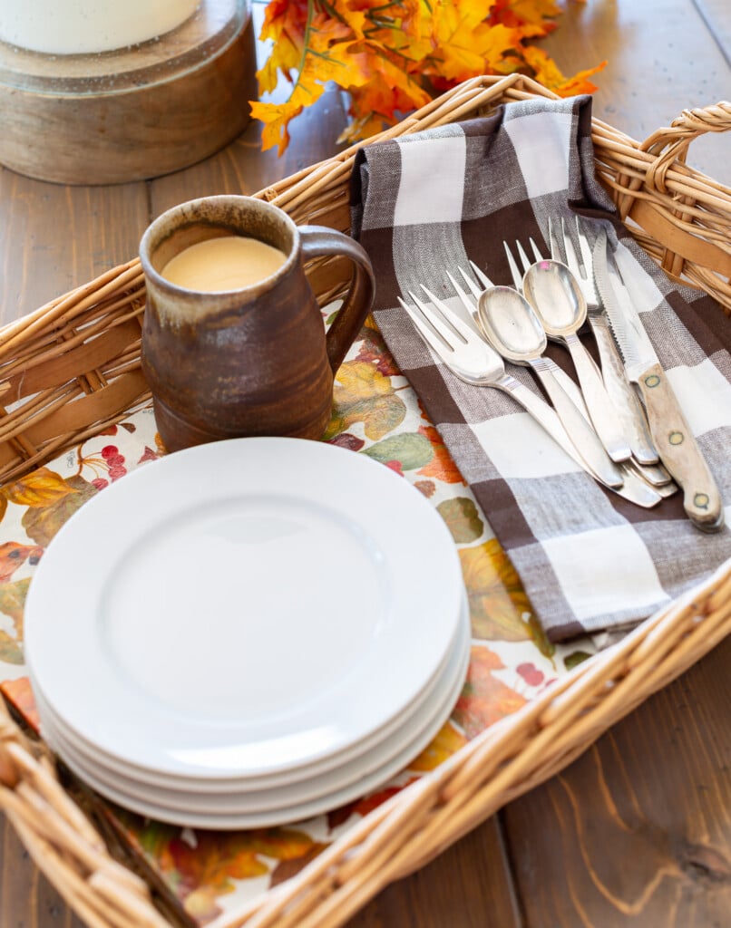 Wicker basket tray completed with autumn leave pattern paper. White plates and brown and white napkin and rustic mug.
