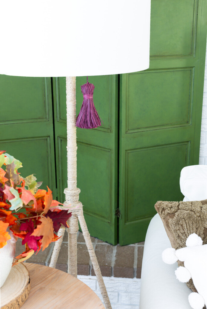 green wooden screen with purple tassel and rope wrapped lamp in front of it showing fall colors of green and purple