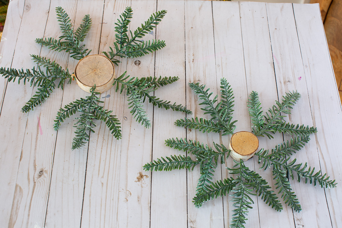 2 tree trunk slice pine star ornaments on work surface.