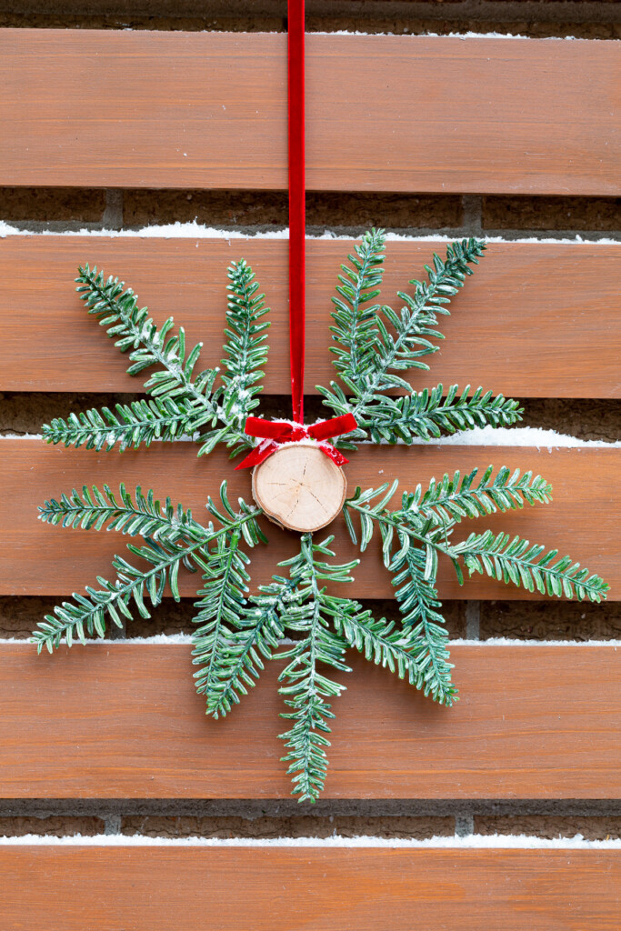 Tree trunk and pine branch Christmas wreath hung on red ribbon outside