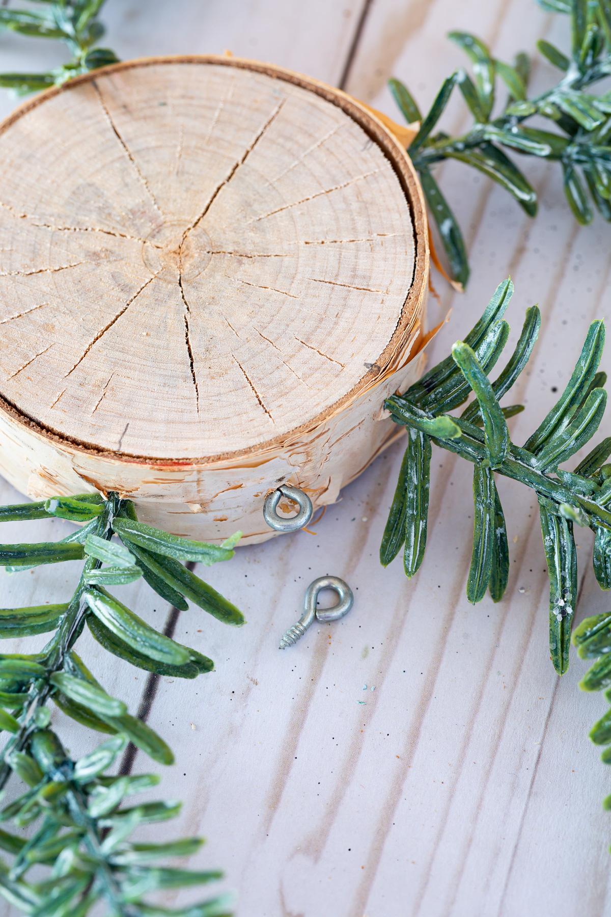 tree trunk slice with pine branches attached to the sides and hook.