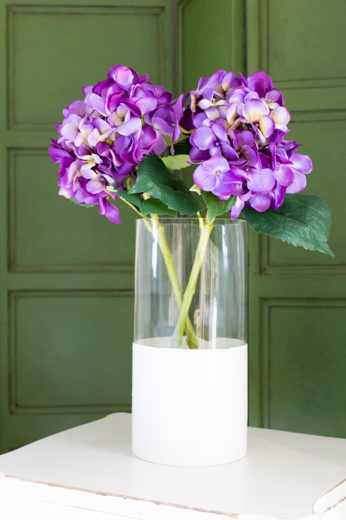 purple hydrangeas in a clear glass vase with bottom half painted white